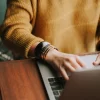 Person using a laptop computer on a desk with a notepad, pen, and smartphone nearby